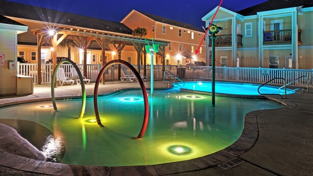 Una piscina con luci colorate, una zona coperta con sedie e un edificio sullo sfondo.
