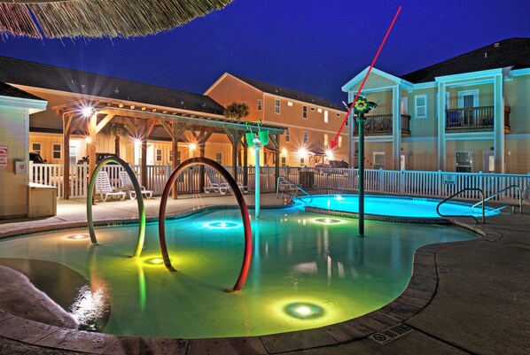 A swimming pool with colorful lights, a covered area with chairs, and a building in the background. - Sleeps 32, 2 Homes | Heated Pool + Game Room + Balconies | Walk to the Beach (Corpus Christi)