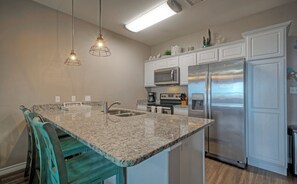 A kitchen with a granite countertop, stainless steel appliances, teal chairs, and pendant lighting. - Sleeps 32, 2 Homes | Heated Pool + Game Room + Balconies | Walk to the Beach (Corpus Christi)