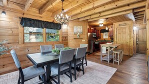 Interno di una baita in legno con sala da pranzo, cucina e un lampadario.