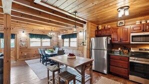 Interno di una baita di legno con zona pranzo, angolo cottura e ampie finestre.