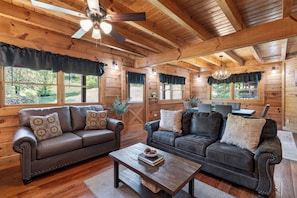 Ein Interieur einer Blockhütte mit zwei Ledersofas, einem Holztisch und einem Deckenventilator.