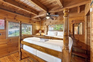 Ein schlichtes Schlafzimmer im Blockhausstil mit einem Himmelbett, einem Deckenventilator und einem Fenster mit Jalousien.