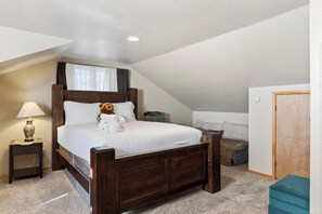 Quarto com cama de madeira, mesa de cabeceira com abajur, uma mesinha e uma porta.