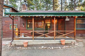 Ein rustikales Blockhaus mit Veranda, einem Willkommensschild und einem Vogelhäuschen.