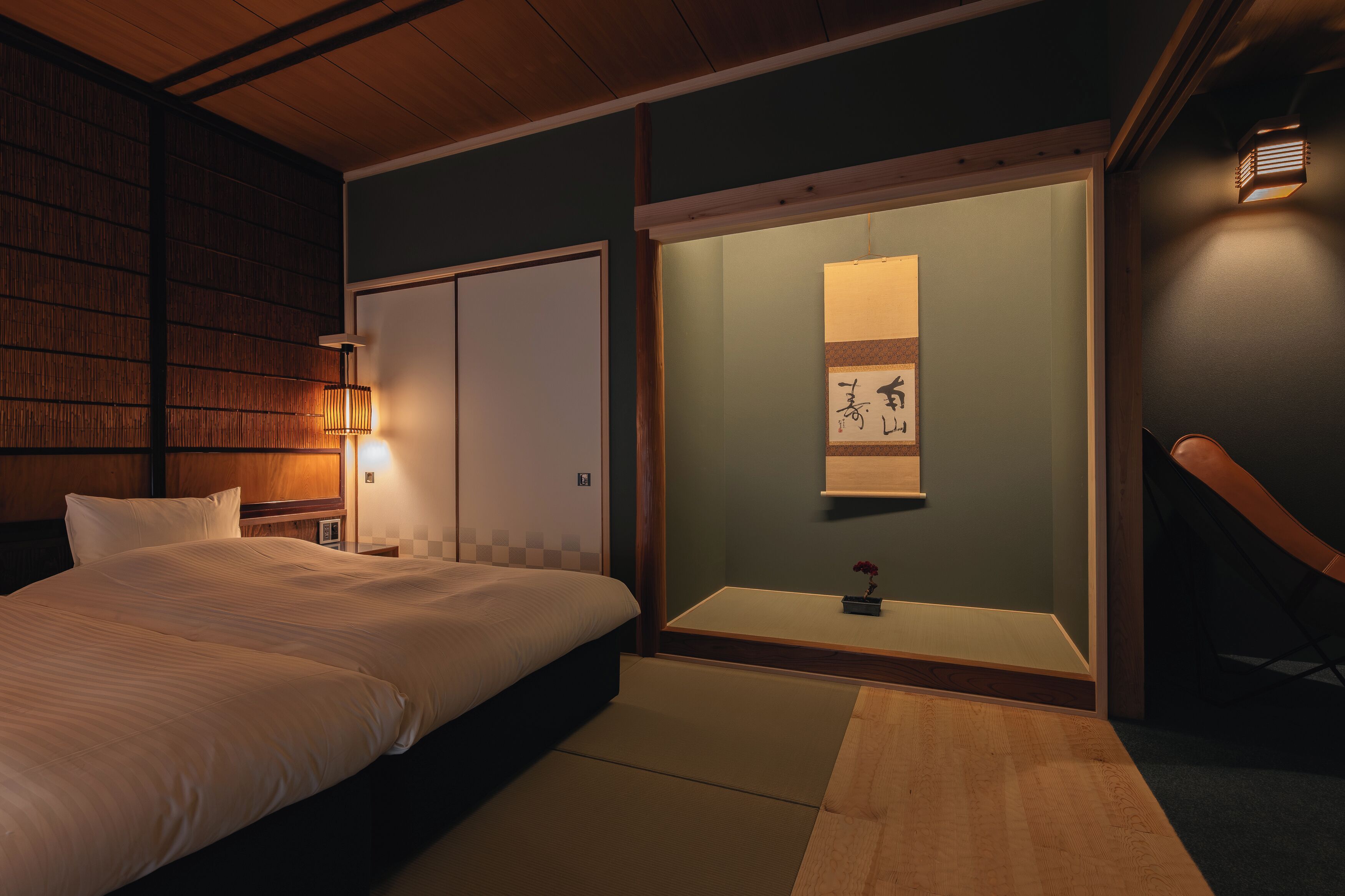 A traditional Japanese-style bedroom with tatami flooring, a bed, a shoji screen, and a wall-mounted light fixture.