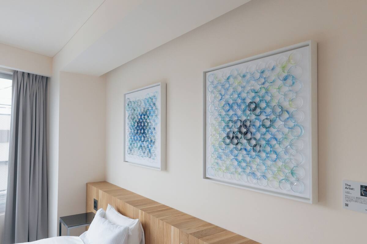 Ein Hotelzimmer mit einem Bett, einem Holz-Kopfteil, einem Nachttisch und zwei gerahmten abstrakten Kunstwerken an der Wand.