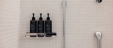 A bathroom with a tiled wall, a chrome showerhead, and a shelf holding three bottles of Fable hand and body wash.