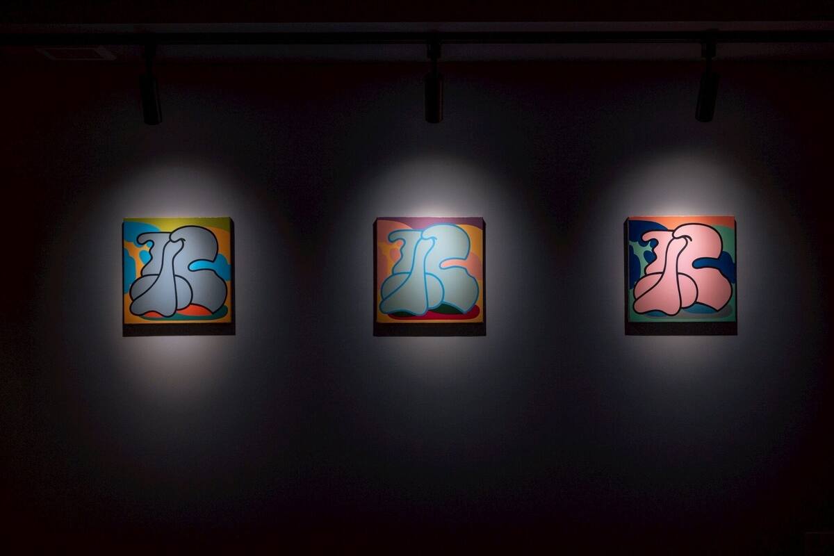 Drei beleuchtete Kunstwerke an einer dunklen Wand.