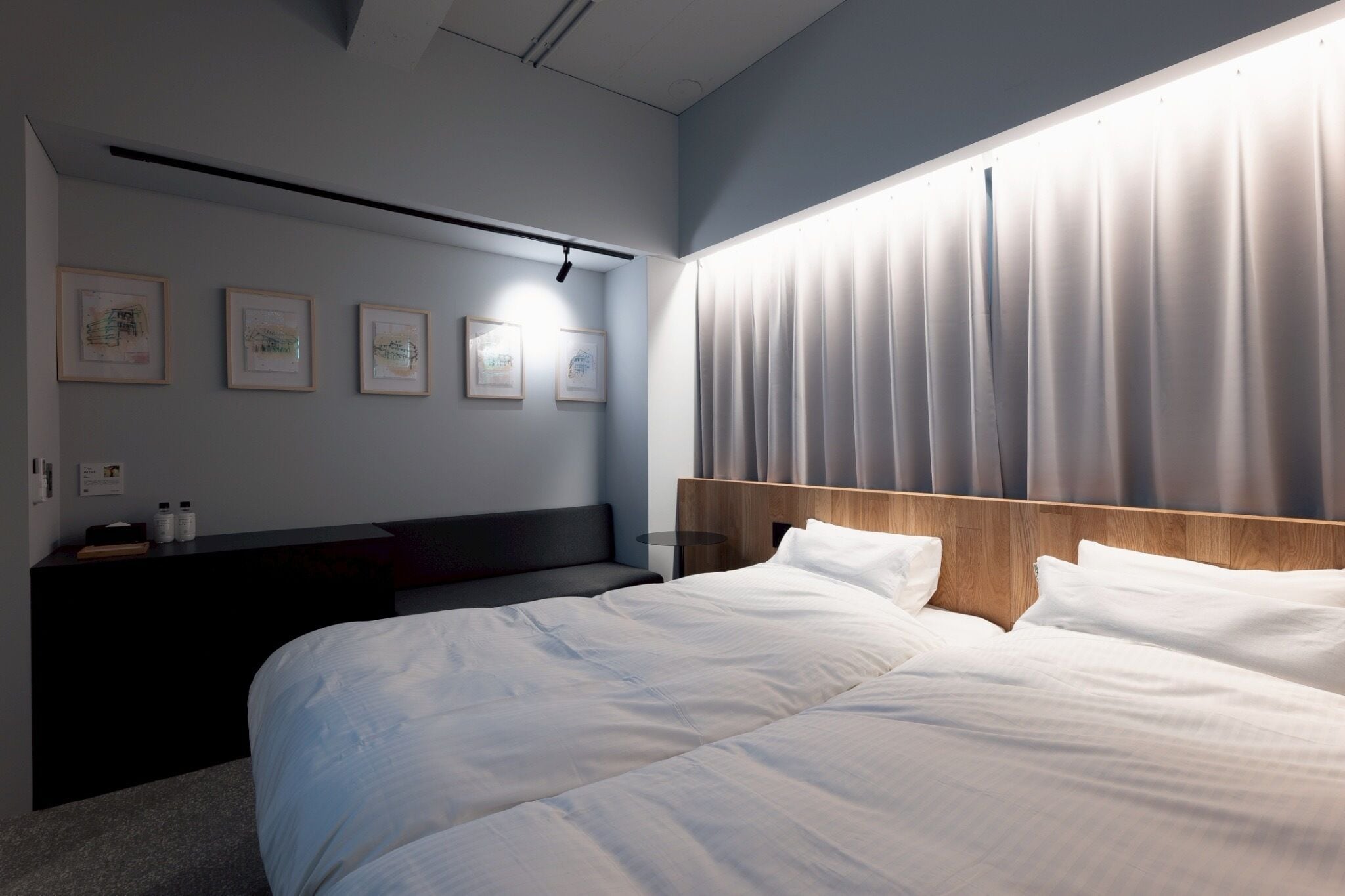 Una habitación de hotel moderna con una cama grande, cabecera de madera y una mesita de noche con lámpara.