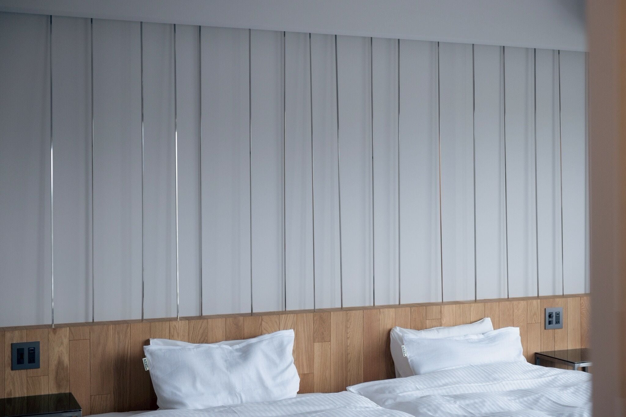 A hotel room with a wooden headboard, two white beds, and a wall with vertical panels.