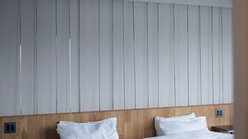 Une chambre d’hôtel avec une tête de lit en bois, deux lits blancs et un mur orné de panneaux verticaux.