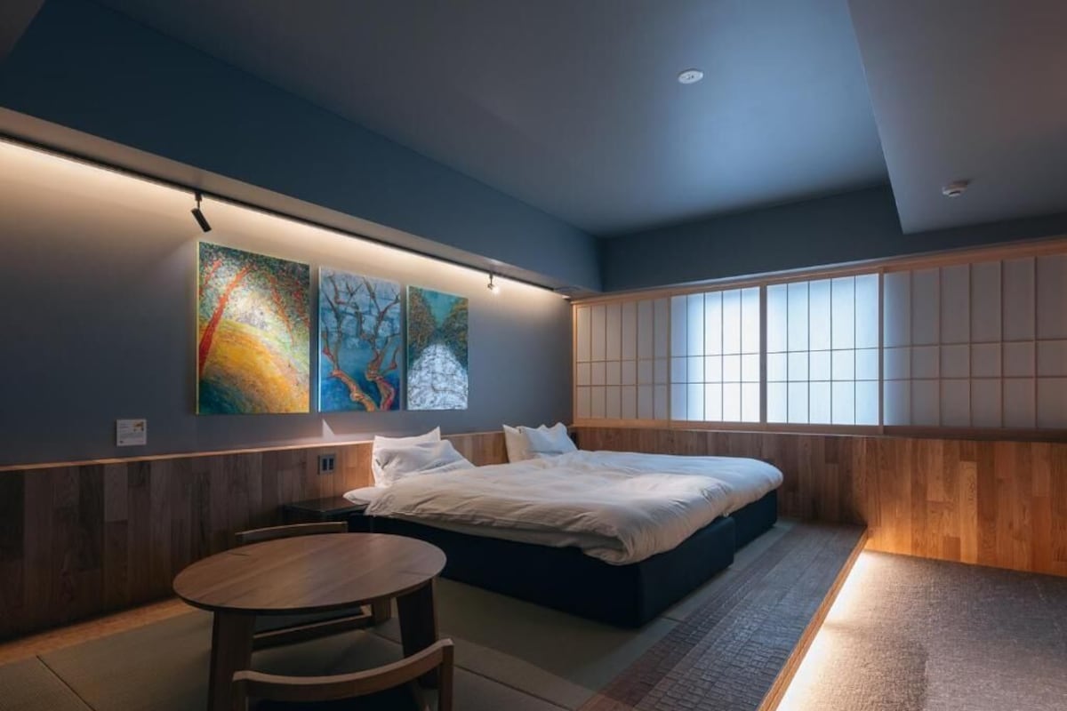 A modern bedroom with a bed, a wooden table, and artwork on the wall.