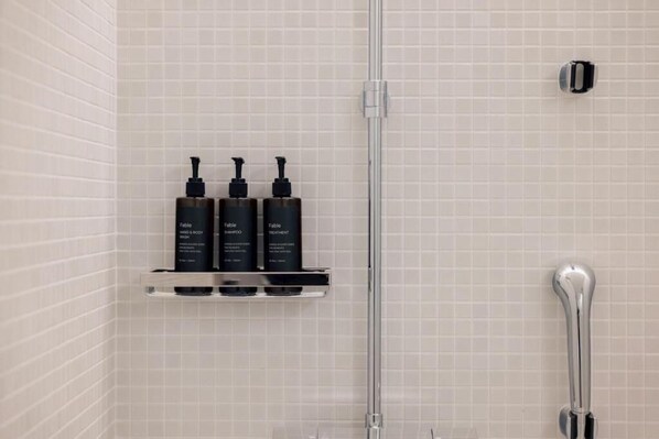 Un baño con pared de azulejos, un cabezal de ducha cromado y tres botellas negras en un estante.