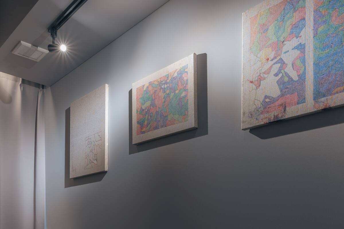 Drei gerahmte Kunstwerke an einer Wand in einer Galerie oder Ausstellungshalle.