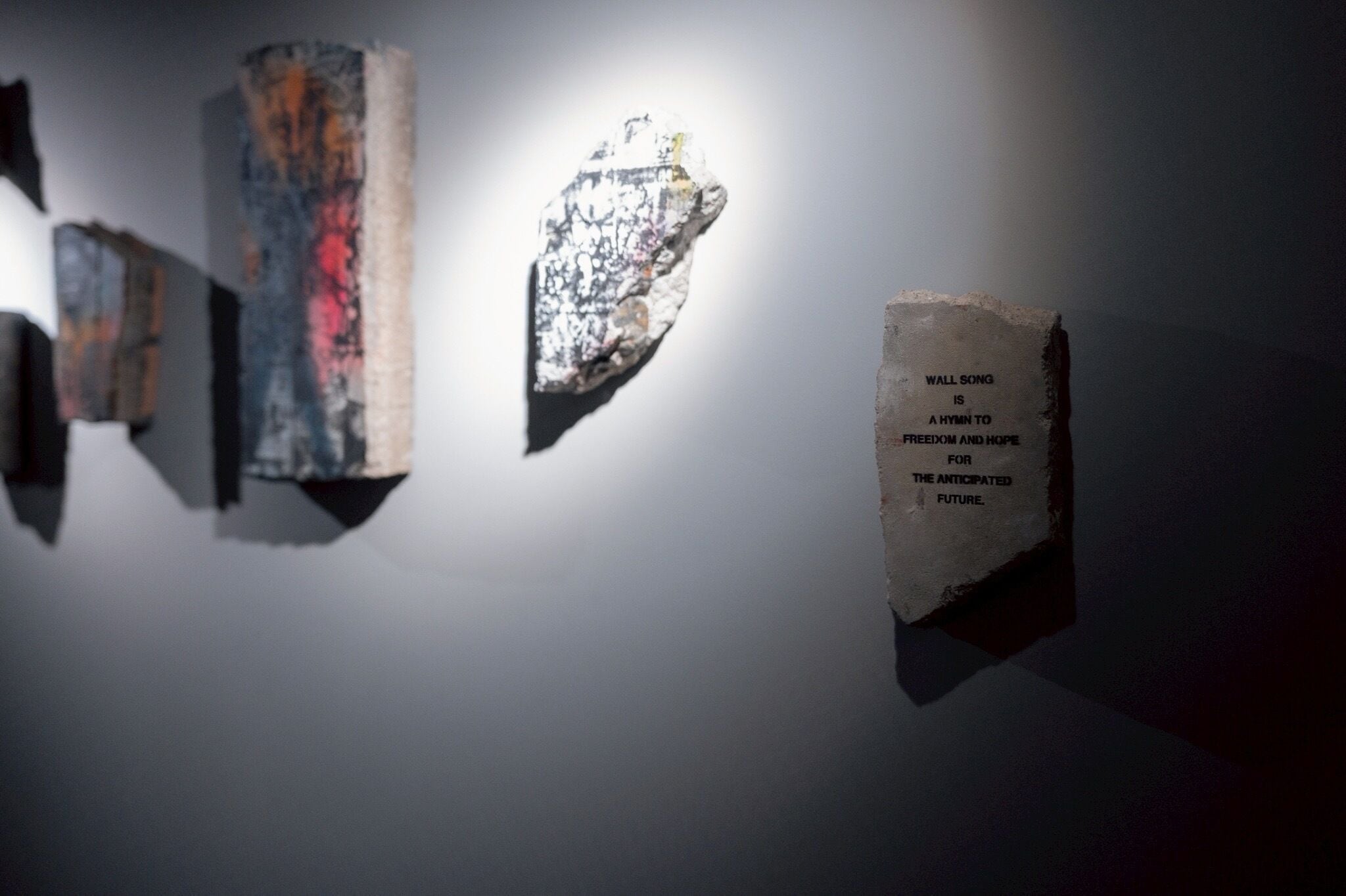 A wall with three textured objects and a plaque with text.