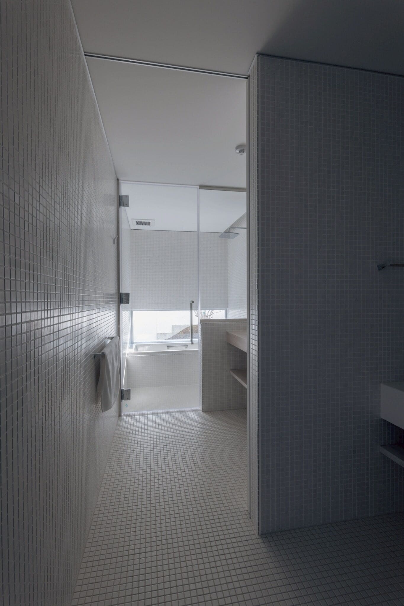 Un baño moderno con suelo de baldosas, cabina de ducha de vidrio y lavamanos blanco.
