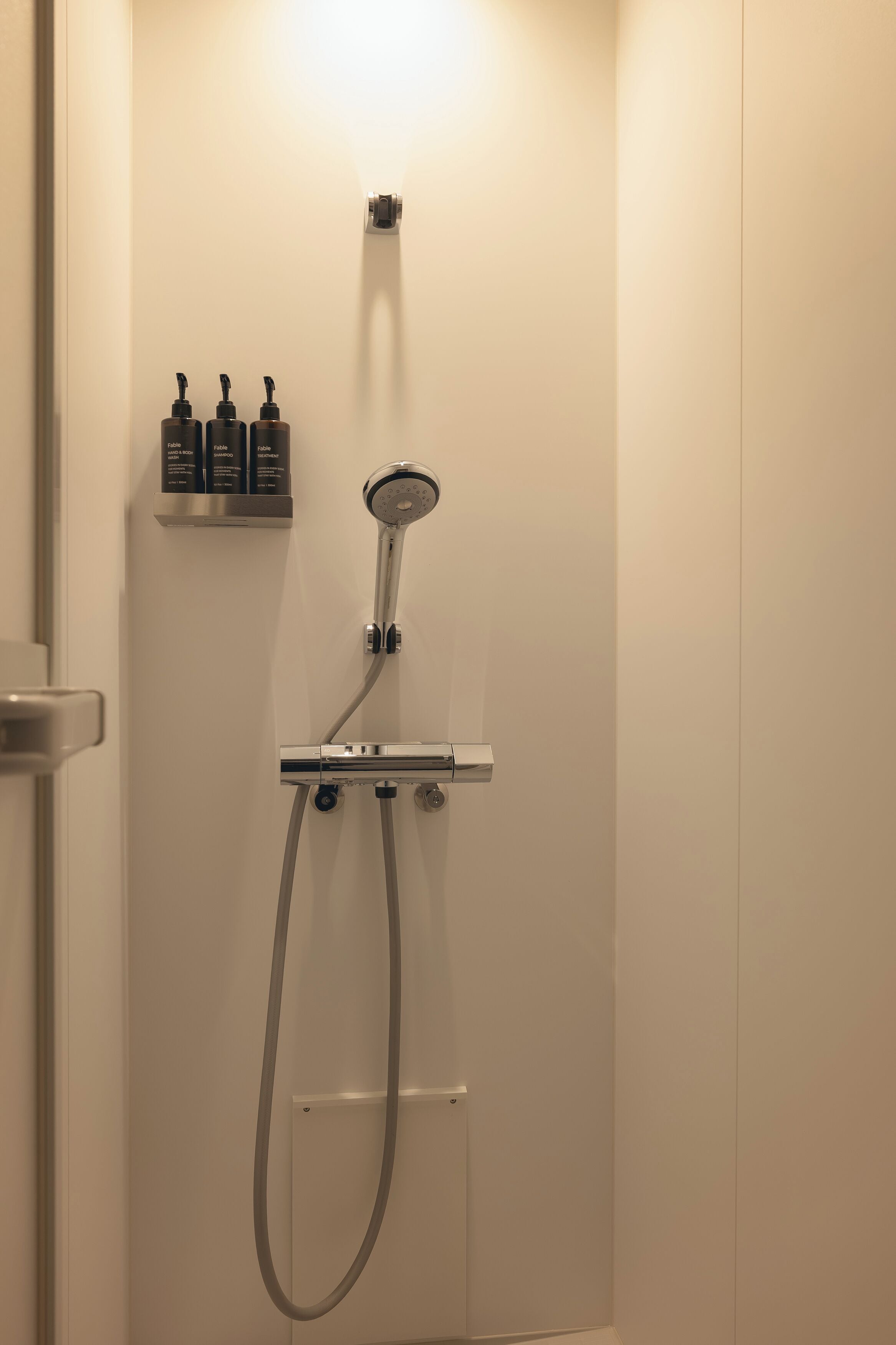 Un baño con ducha, dispensador de jabón para manos y cuerpo, y un perchero para toallas.