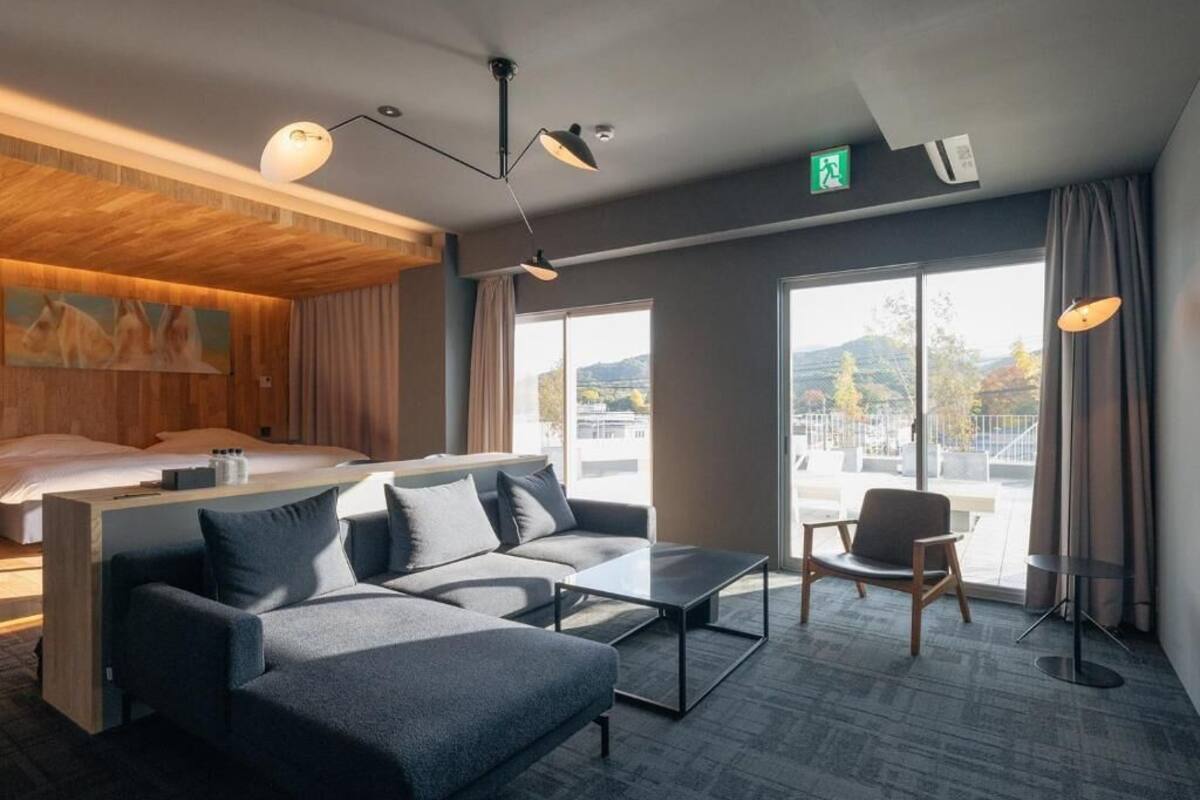 Ein modernes Hotelzimmer mit einer Couch, einem Couchtisch, einem Sessel, einem Bett und großen Fenstern mit Blick.