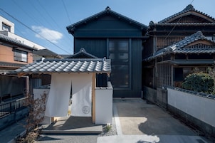 Una casa japonesa tradicional con techo de tejas, un pequeño porche y una valla de madera.