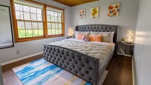 A bedroom with a tufted headboard, a large window, and artwork on the wall.