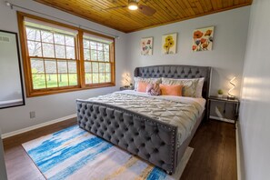 A bedroom with a tufted headboard, a large window, and artwork on the wall.