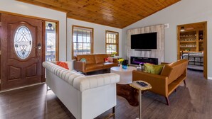 A living room with a wooden ceiling, a fireplace, a TV, and a dining area with a wooden table and chairs.