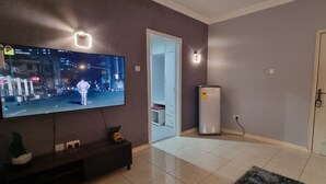 Een woonkamer met een televisie, een koelkast, een deur en een betegelde vloer.