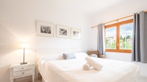 Quarto com cama, mesa de cabeceira, abajur e três quadros na parede.