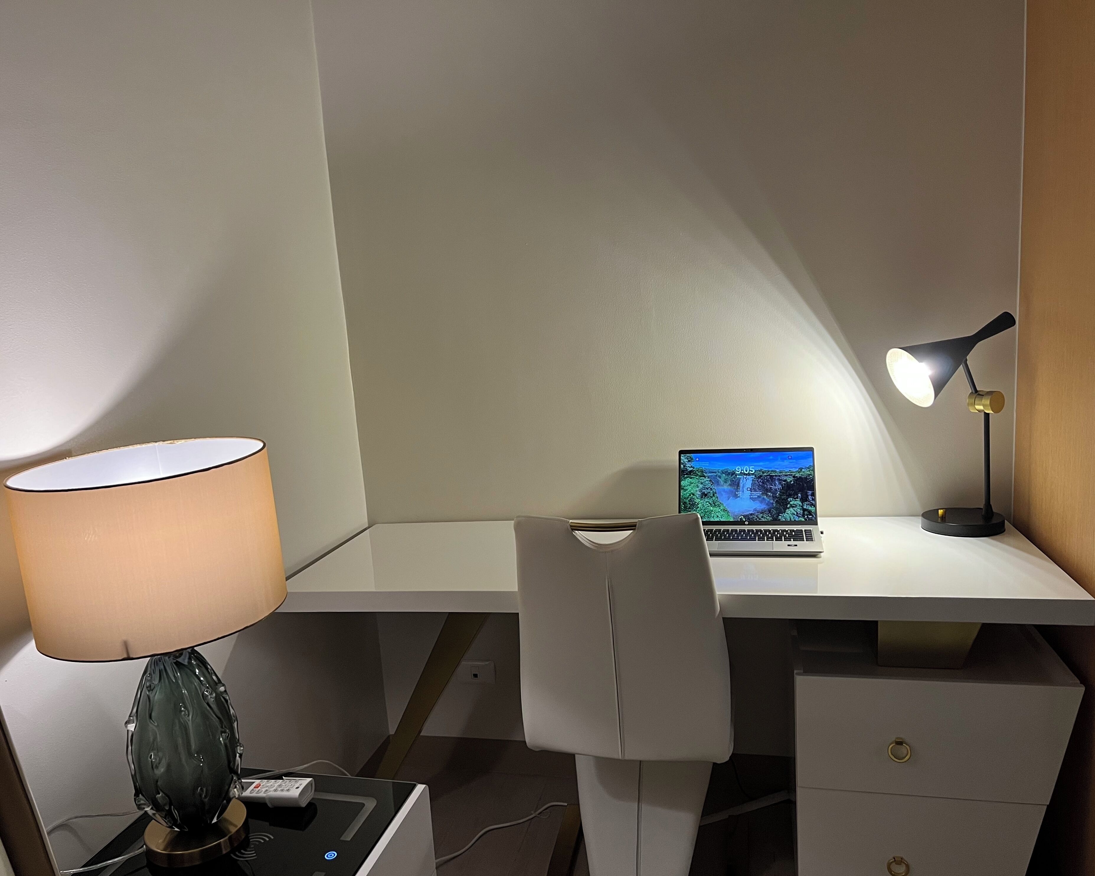 A workspace with a desk, a laptop, a lamp, and a chair.
