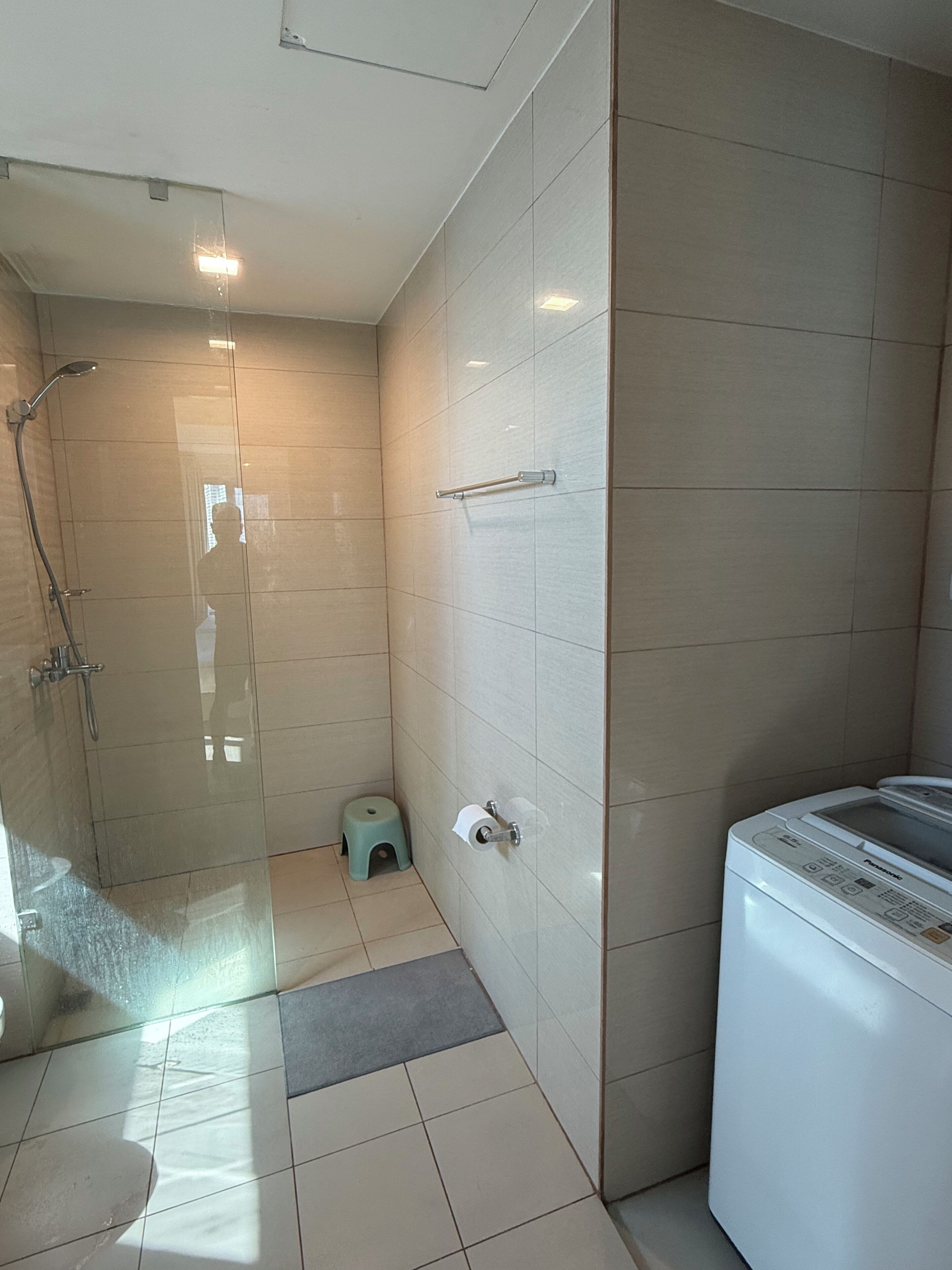 A modern bathroom with a glass shower enclosure, a toilet paper holder, and a washing machine.