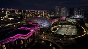 Un edificio grande y moderno con estructura en forma de cúpula, rodeado de paseos iluminados y áreas de estacionamiento.