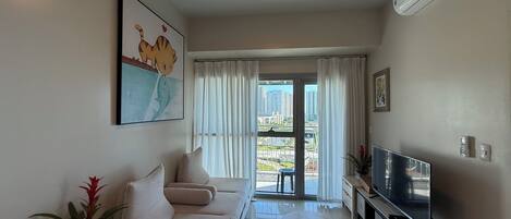 A modern living room with a sofa, TV, and a view of the city through large windows.
