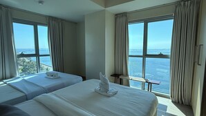 Habitación de hotel con dos camas, una mesita y vista al océano.