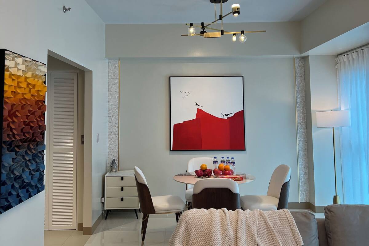 A modern living room with a gray sofa, a dining table with fruit, and a unique ceiling light fixture.