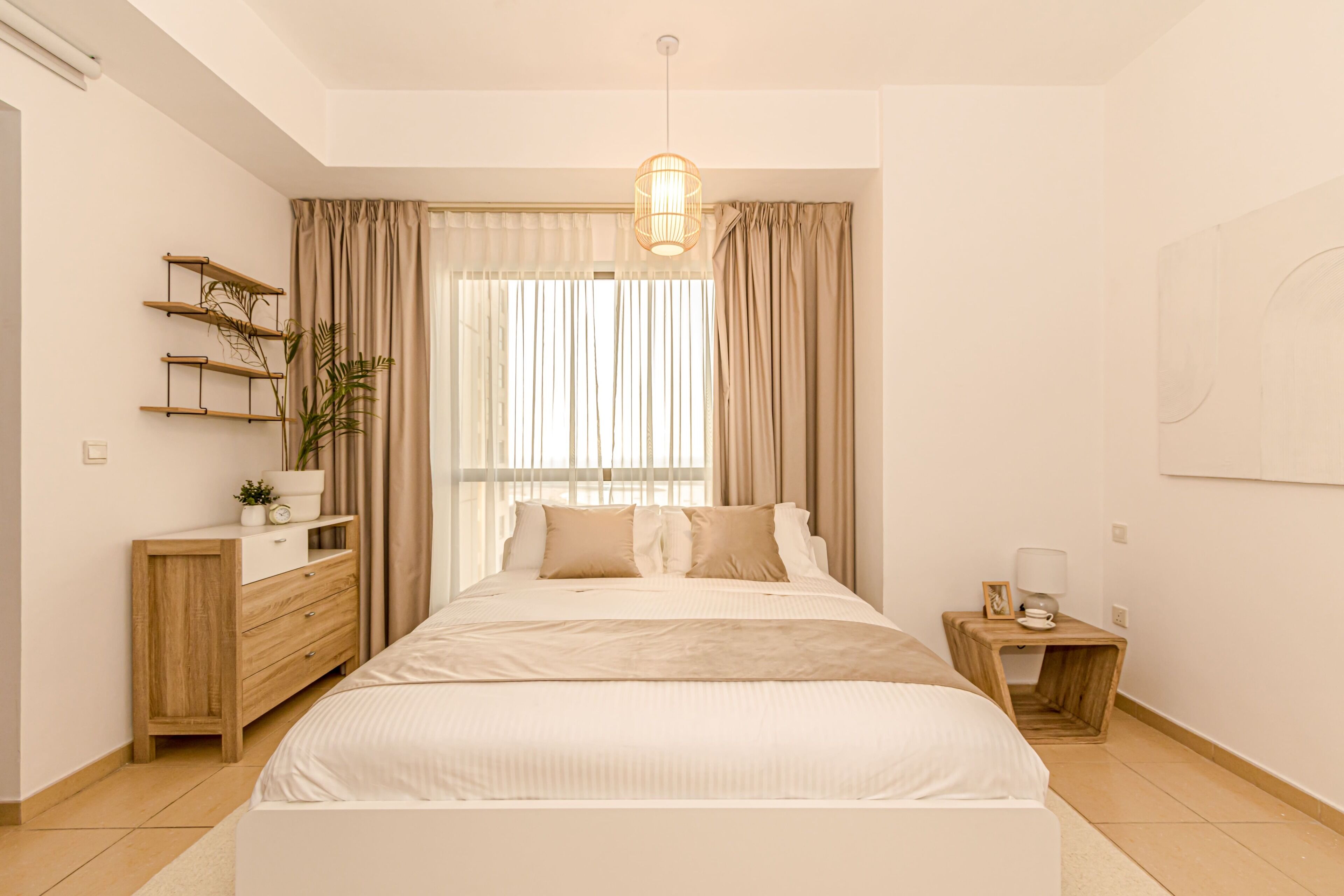 Een slaapkamer met een bed, nachtkastjes, een dressoir, een hangplant en een raam met gordijnen.