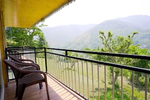 Un balcón con sillones de mimbre, piso de madera y vistas a colinas verdes.