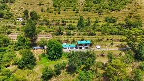 A two-story house with a green roof, surrounded by lush greenery and terraced fields. - Kabila King Resort (Chakrata)