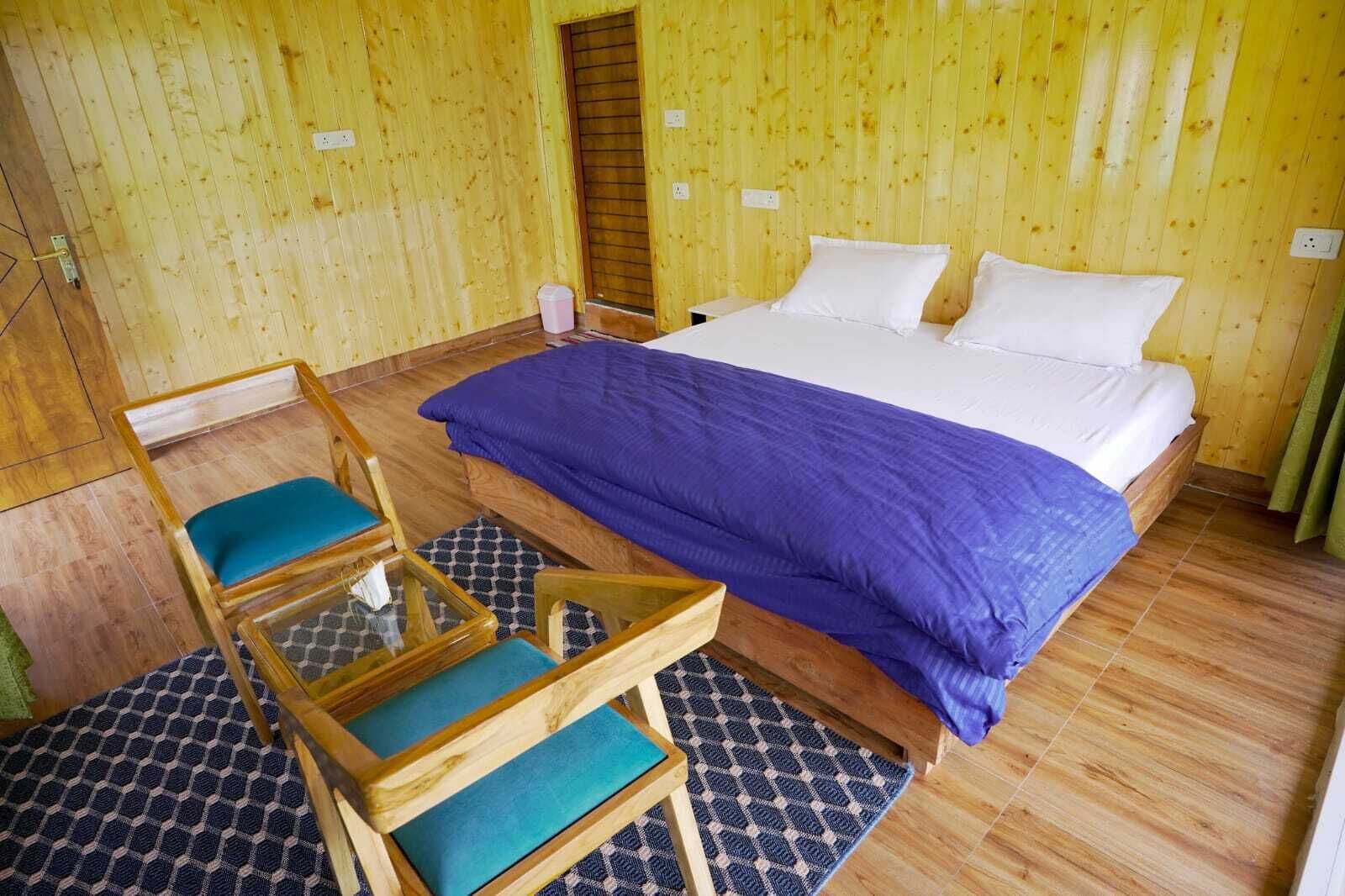 Una habitación con paneles de madera, una cama, dos sillas y un tapete estampado.