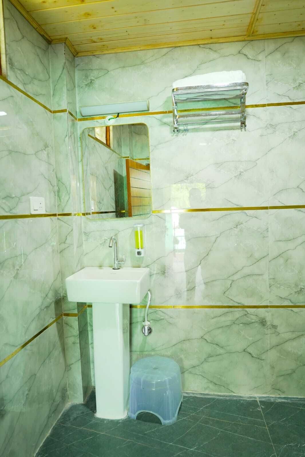 Ein Badezimmer mit Waschbecken, Spiegel, Handtuchhalter und einem kleinen Hocker.