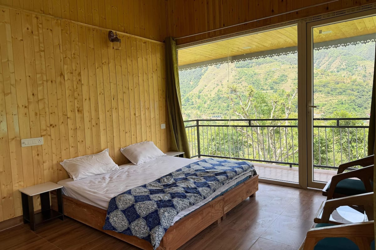 A wooden room with a bed, a nightstand, and a view of a mountainous landscape through a balcony.