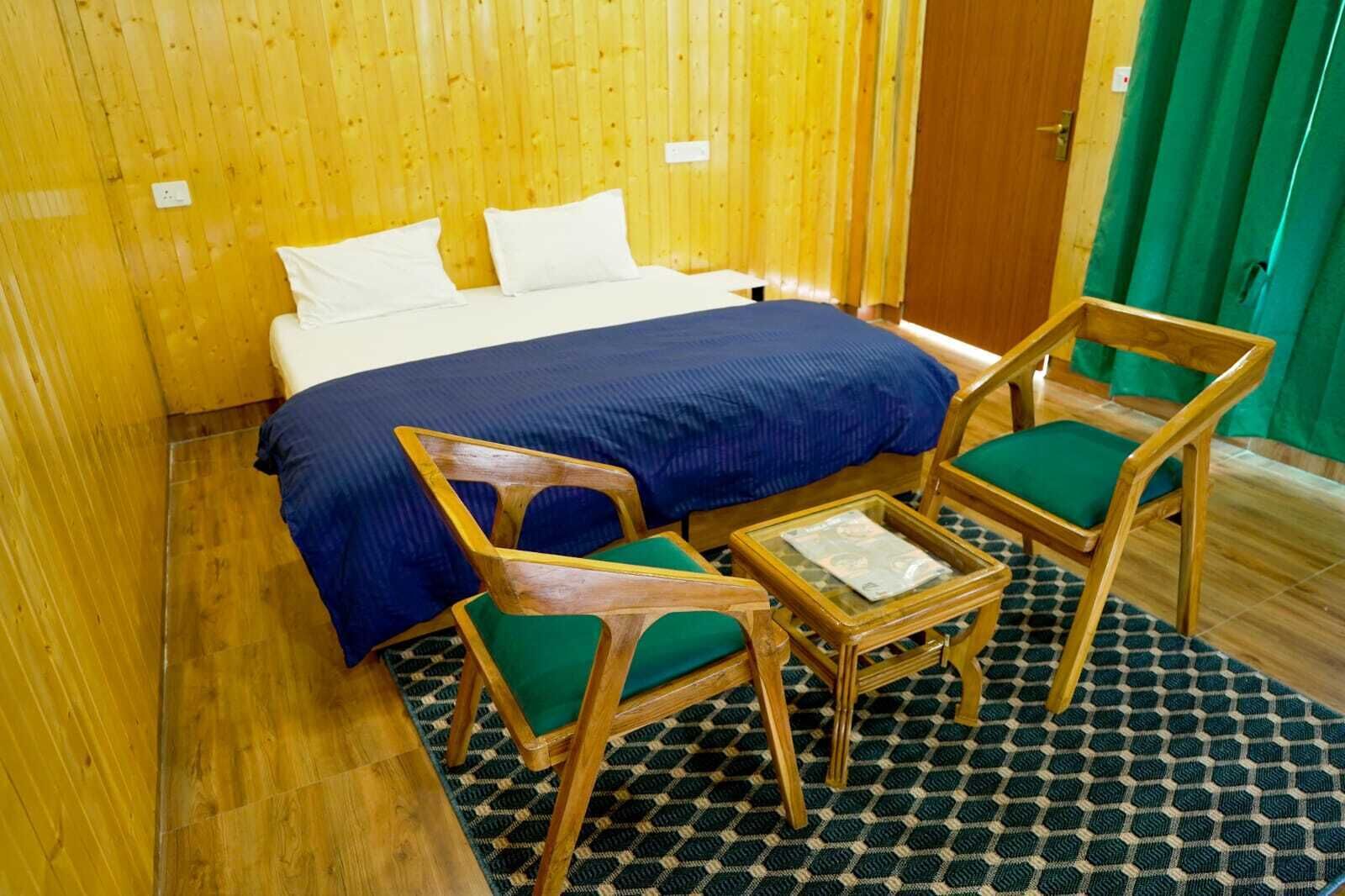 Ein Zimmer mit einem Bett, zwei Stühlen, einem kleinen Tisch und einem gemusterten Teppich.