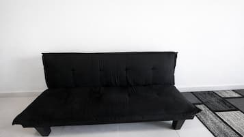 Un sofá negro con respaldo capitonado y cuatro patas, colocado frente a una pared blanca con un tapete estampado en el suelo.
