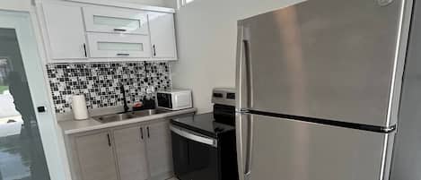 A modern kitchen with stainless steel appliances, white cabinetry, and a black and white tiled backsplash.