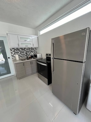 A modern kitchen with stainless steel appliances, white cabinetry, and a black and white tiled backsplash. - Charming and Private Stay in Fajardo - Near Ferry - Beaches - EL Yunque - Biobay (Fajardo)