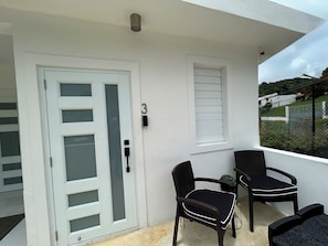 A balcony with a white door, two wicker chairs, and a small potted plant. - Charming and Private Stay in Fajardo - Near Ferry - Beaches - EL Yunque - Biobay (Fajardo)