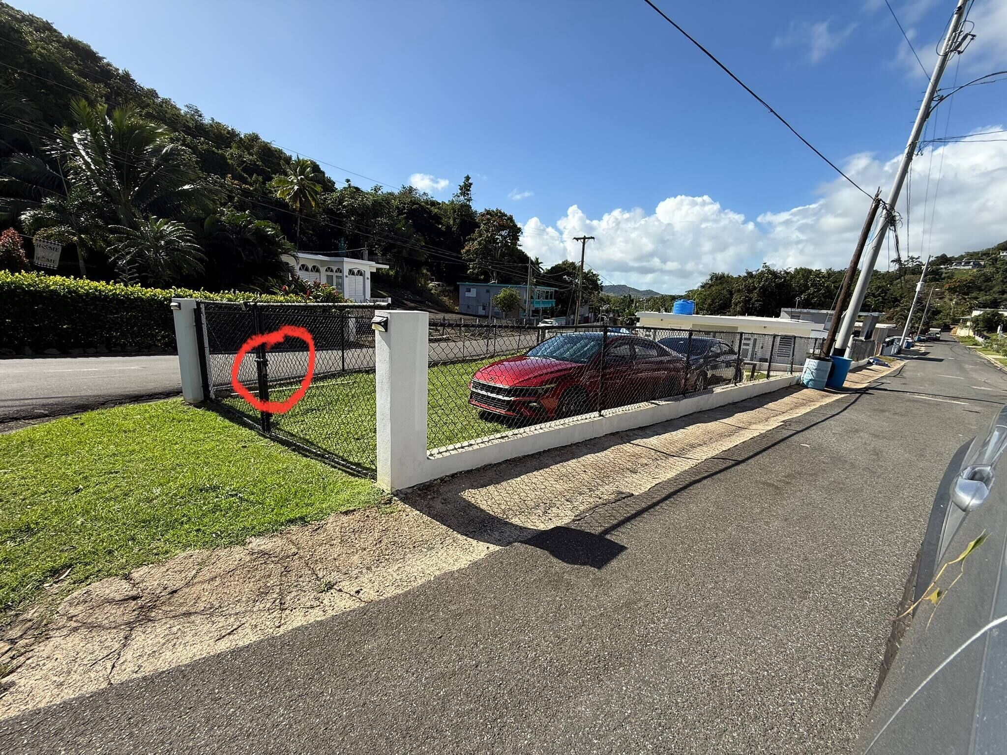 A fenced parking area with a red car inside, a grassy area, and a clear sky.