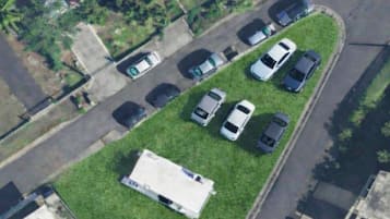 An aerial view of a parking lot with several cars parked, a grassy area, and a building with a flat roof.