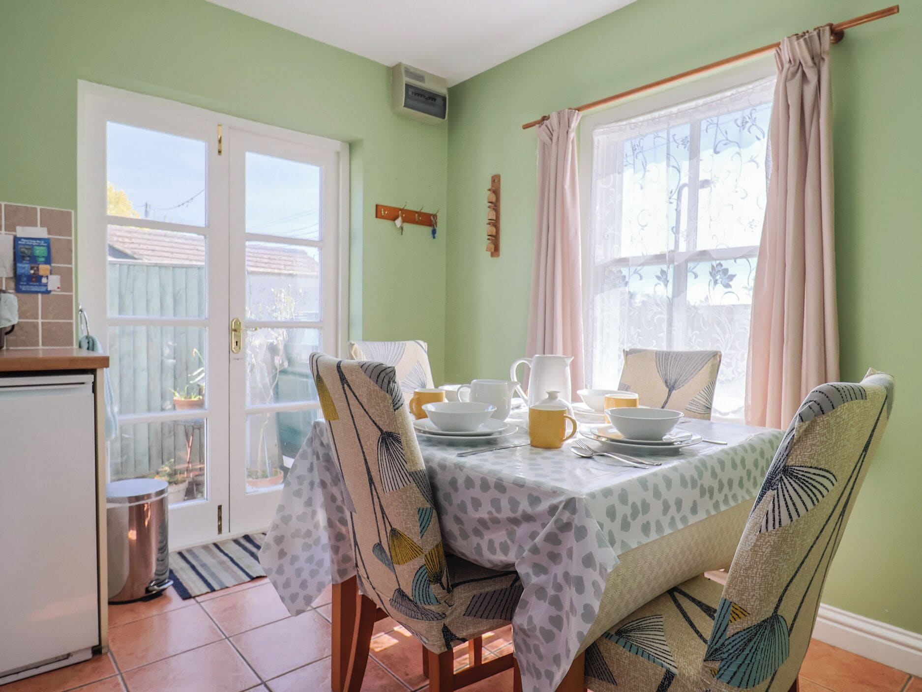 Un coin repas avec une table dressée pour quatre personnes, des chaises à l  ’assise recouverte d’un tissu à motifs, une fenêtre avec des rideaux et une vue sur l’extérieur.