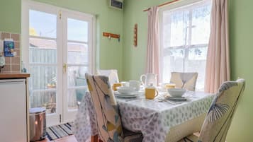 A dining area with a table set for four, chairs with patterned upholstery, a window with curtains, and a view of the outside.